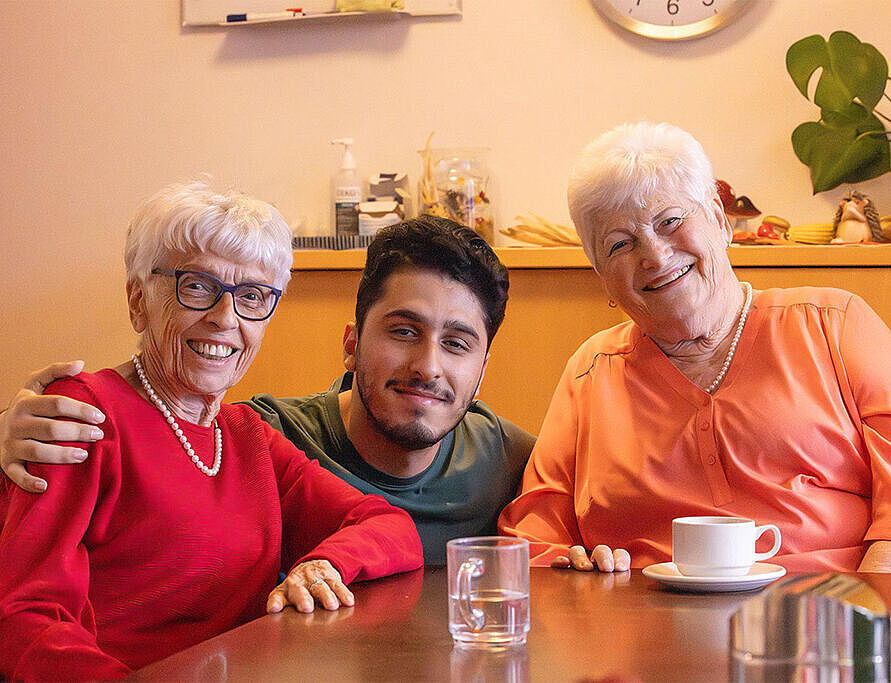 Pflegekraft verbringt gemeinsam mit zwei Bewohnerinnen eine gemütliche Kaffeepause am Nachmittag.
